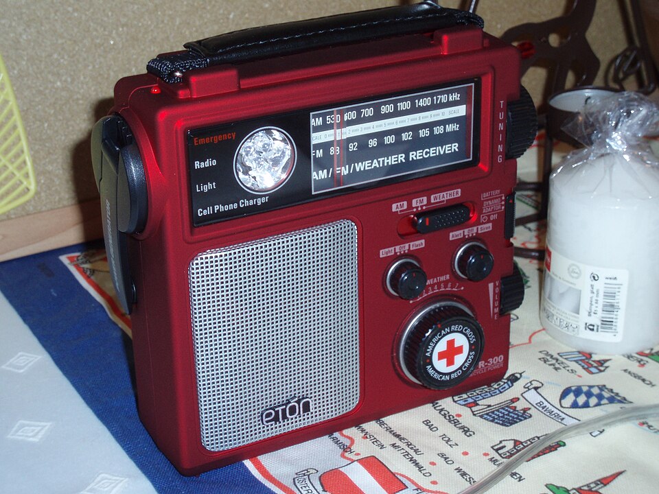 A red Eton emergency radio with a tuning dial, speaker grille and hand crank, for storm prep in Coralville, IA